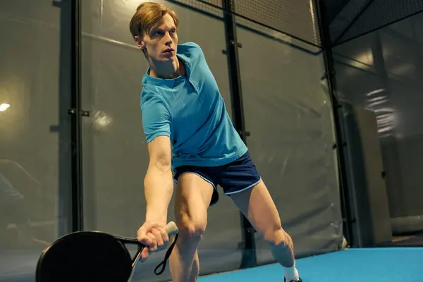 A focused young athlete performs a powerful shot on the padel court, showcasing agility. — Stock Photo