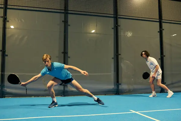 Two young men showcase their skills while playing padel on a bright blue court. — Stock Photo