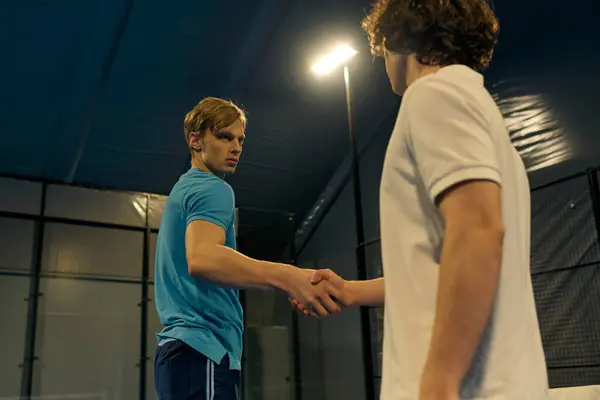 Two young men in sportswear shake hands after playing padel in the indoor court. — Stock Photo