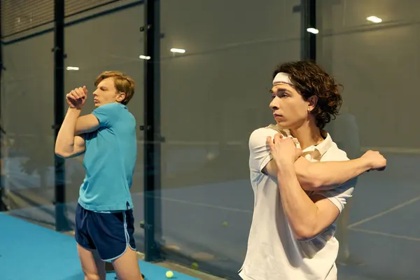Two young men warm up with stretches on a padel court preparing for their match today. — Stock Photo