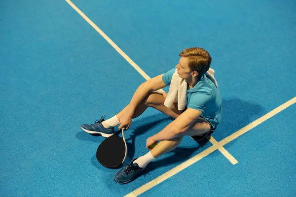 A young athlete rests on the court after an intense game of padel. He reflects on his performance. — Stock Photo