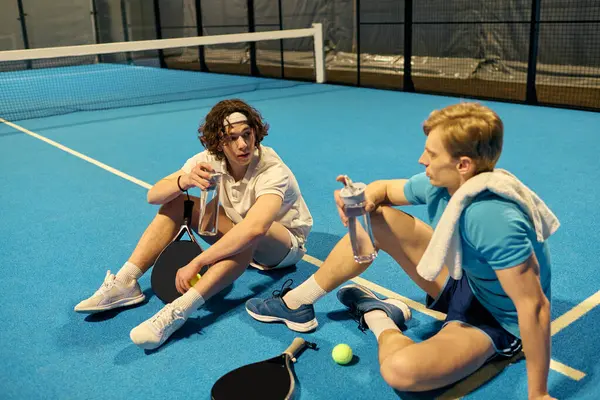 Due giovani in abbigliamento sportivo si prendono una pausa, godendosi l'acqua dopo un intenso gioco di padel. — Foto stock