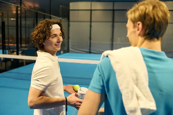 Two young men enjoy a light chat as they prepare for their padel game, showing camaraderie. — Stock Photo