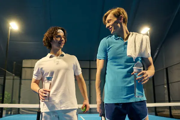 Two young men engage in friendly banter after an exciting padel match at an indoor court. — Stock Photo