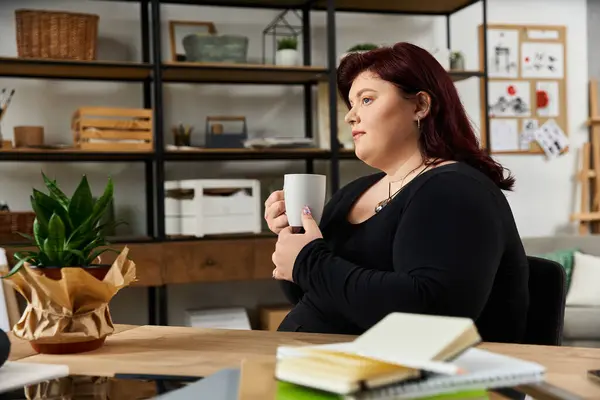 Una donna chic si gode una bevanda calda contemplando il suo processo artistico in uno studio vibrante. — Foto stock
