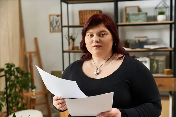 Schicke Frau hält Papiere in der Hand, während sie von einem inspirierenden Atelier voller Kreativität umgeben ist. — Stockfoto