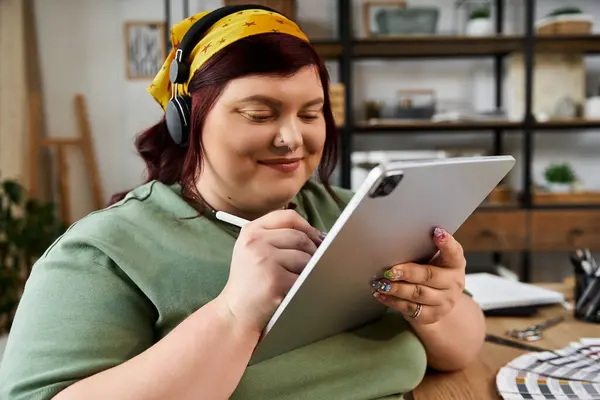 Una mujer bonita inmersa en sus obras de arte, hábilmente usando una tableta con un enfoque en la creatividad. - foto de stock