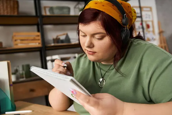 Pretty woman listens to music while sketching ideas in a cozy art studio, immersed in creativity. — Stock Photo
