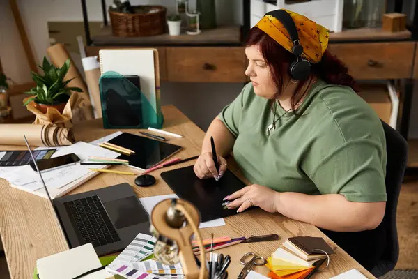 En un acogedor estudio de arte, una mujer se concentra en su tableta en medio de materiales y diseños. - foto de stock