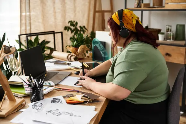 A pretty woman wearing headphones engages deeply in creating sketches at her artistic work station. — Stock Photo