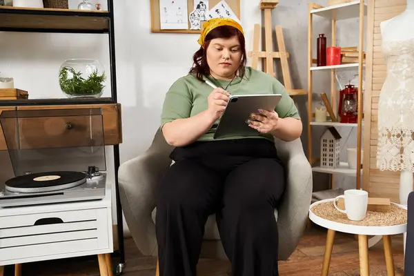 Comprometida con la expresión creativa, una mujer elegante se sienta en un acogedor estudio de arte, dibujando en una tableta. - foto de stock