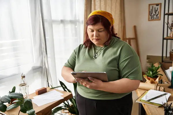 A stylish woman engages with her tablet in a cozy art studio filled with plants and artwork. — Stock Photo