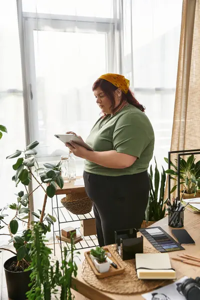 Una mujer elegante trabaja en su arte en un vibrante estudio lleno de plantas. - foto de stock