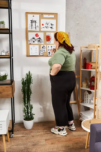 A stylish woman reflects on her artistic choices in a sunlit studio filled with art. — Stock Photo