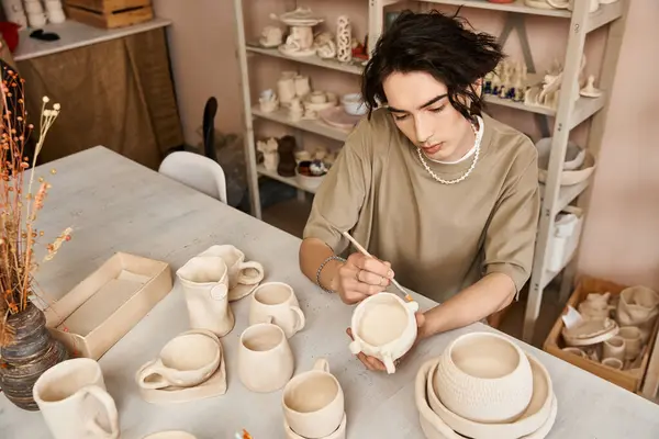 Handsome man carefully decorates a handmade ceramic piece in a lively pottery studio. — Stock Photo