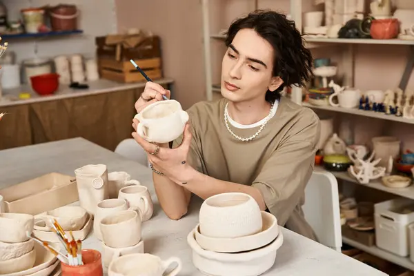 A handsome man paints intricate designs on a fresh pottery piece amid artistic creations. — Stock Photo
