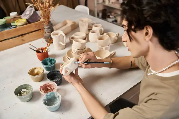 An artist skillfully shapes pottery amidst vibrant glazes and tools in their studio. — Stock Photo