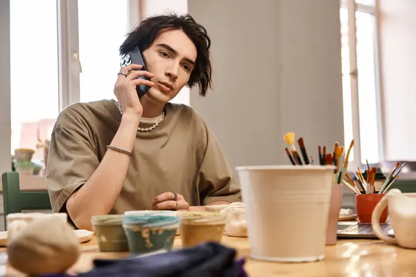 Handsome man connects on the phone while surrounded by colorful pottery materials in the studio. — Stock Photo