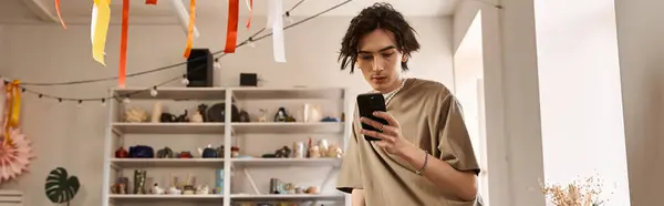 Handsome man in a pottery studio engrossed in his phone, inspiration surrounds him everywhere. — Stock Photo