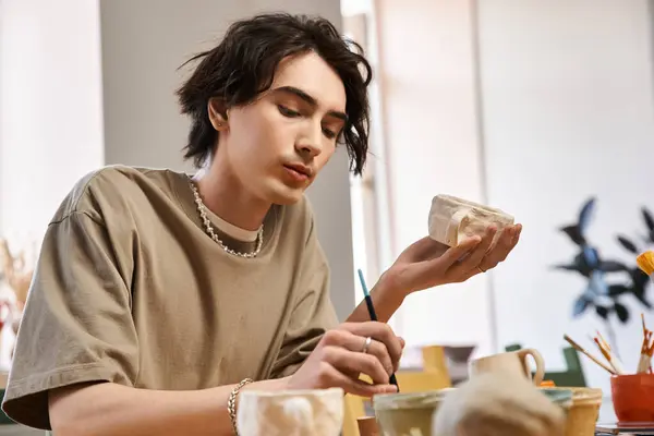 Un hombre guapo forma hábilmente la cerámica mientras está rodeado de herramientas artísticas en un estudio vibrante. - foto de stock