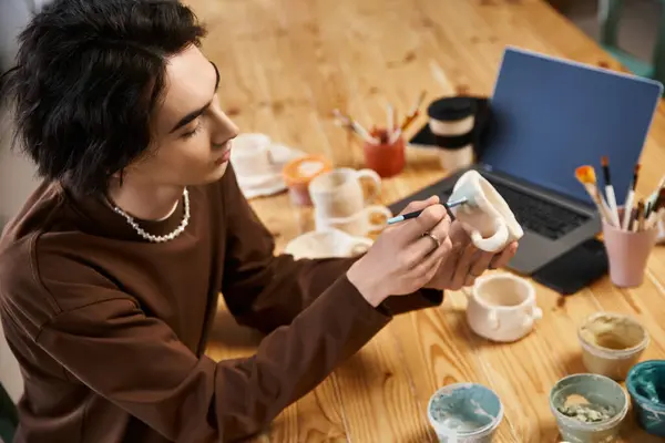 Handsome man focuses on designing a unique ceramic piece amid a vibrant pottery studio. — Stock Photo