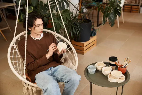A fashionable man focuses on shaping pottery in a bright and inviting studio filled with plants. — Stock Photo