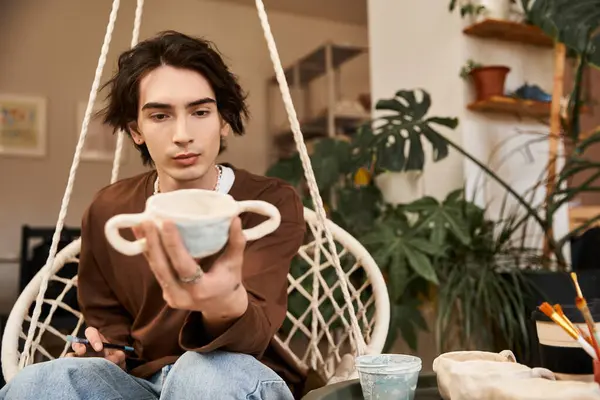 Creative man carefully examines his handmade pottery while surrounded by artistic materials. — Stock Photo