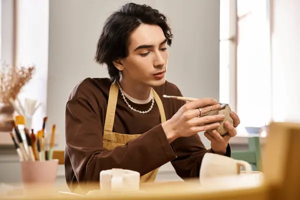 A man delicately paints a ceramic piece in his inviting pottery studio filled with creativity. — Stock Photo