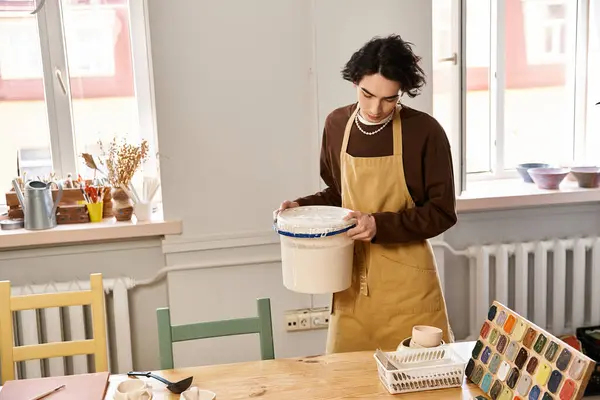 A talented man in an apron engages with pottery materials in a sunlit studio filled with creativity. — Stock Photo
