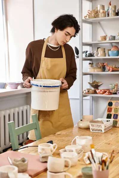 Hombre guapo con un delantal examina cuidadosamente los materiales de cerámica en un estudio vibrante - foto de stock