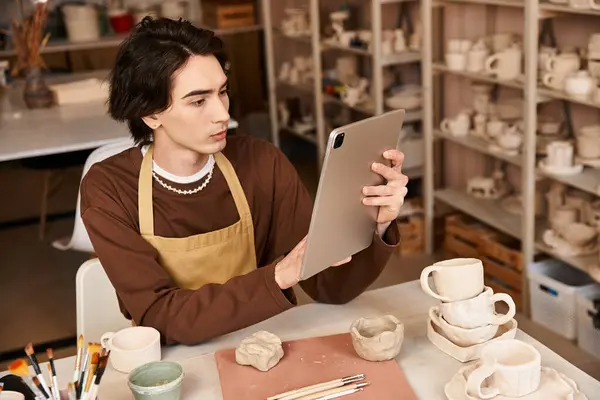 Stylish man engaged in pottery work, drawing inspiration from digital tools in an artistic setting. — Stock Photo