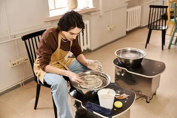 Stylish man focused on shaping clay at a pottery wheel in a vibrant studio filled with creativity. — Stock Photo
