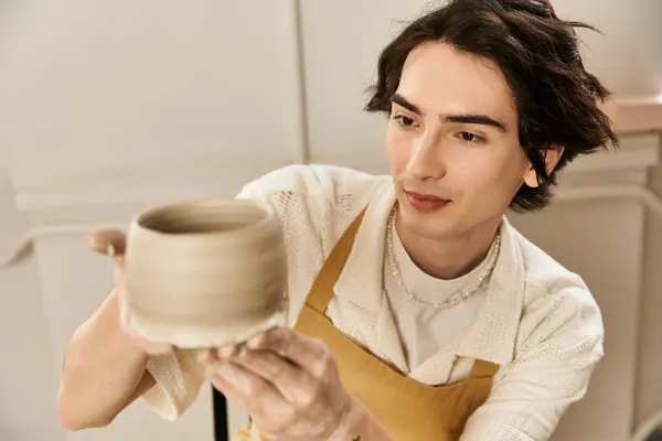 In a vibrant pottery studio, a handsome man skillfully molds a clay bowl, radiating creativity. — Stock Photo