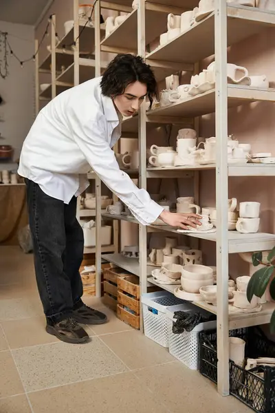 In a pottery studio, a stylish man arranges ceramics on shelves, highlighting creativity. — Stock Photo