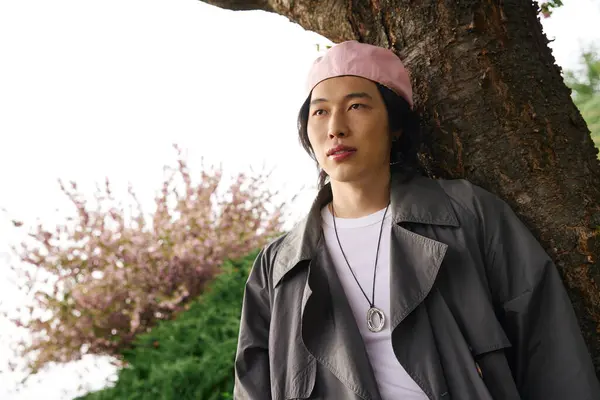 A young asian man relaxes in a vibrant park, showcasing a trendy grey outfit perfect for spring. — Stock Photo