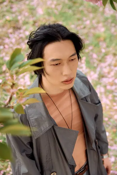 A young Asian man enjoys a peaceful moment in a park, surrounded by blooming flowers. — Stock Photo