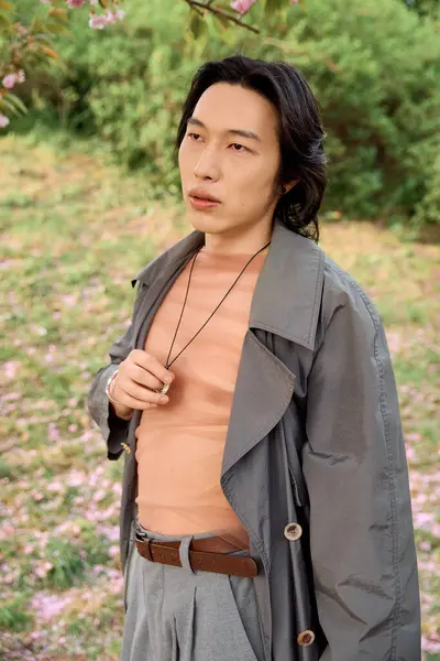 A young asian man enjoys a serene moment in a park wearing a stylish grey outfit, embracing nature. — Stock Photo