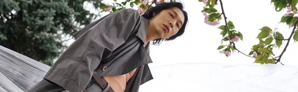 A young Asian man displays modern fashion while walking in a serene park among trees, banner — Stock Photo