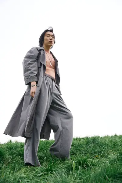 A young Asian man models his stylish grey outfit on green grass, enjoying the outdoors. — Stock Photo