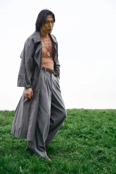 A young Asian man walks confidently in a stylish grey outfit while exploring a vibrant park. — Stock Photo