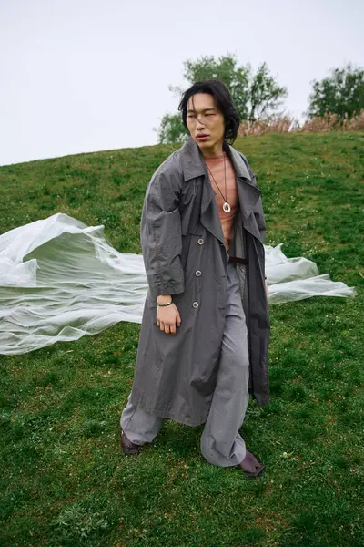 A young asian man showcases a trendy grey outfit in a vibrant park setting near polyethylene — Stock Photo