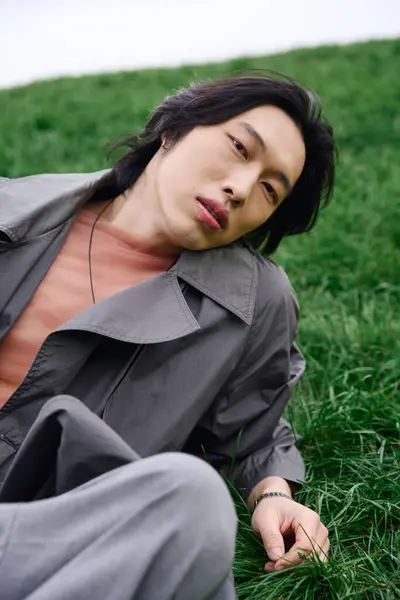 Ein junger asiatischer Mann in modischem grauen Outfit sitzt in einem wunderschönen Park und genießt die Natur. — Stockfoto