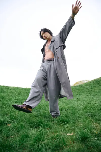 A young man in a grey trench coat displays confidence while posing in a lush park. — Stock Photo