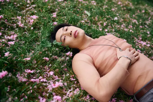 A young Asian man relaxes on the grass, surrounded by blooming flowers in a stylish outfit. — Stock Photo