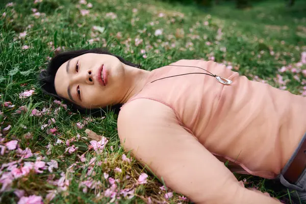 A young man relaxes on the grass, dressed in a fashionable outfit, surrounded by blossoms. — Stock Photo