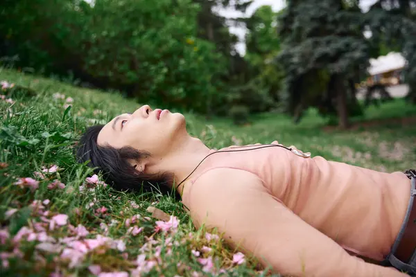 A young asian man enjoys a peaceful moment in the park, lying on the grass in style. — Stock Photo