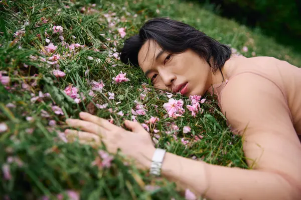 A young asian man rests on grass surrounded by flowers — Stock Photo