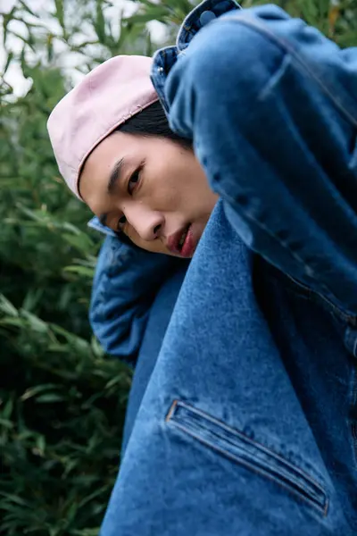 A young asian man showcases a trendy denim outfit in a lively park setting, exuding confidence. — Stock Photo