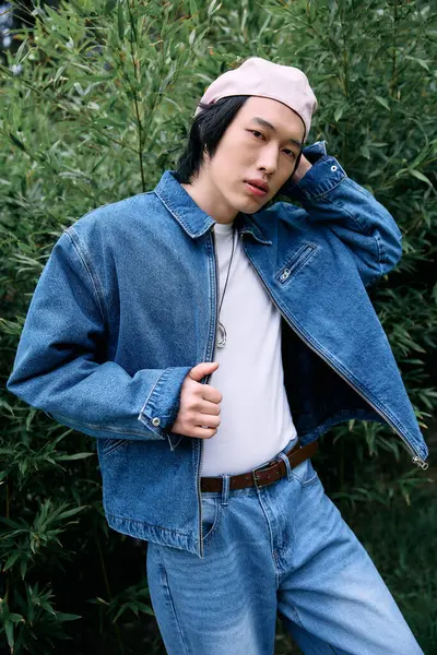 Un joven asiático posa con confianza en un traje de mezclilla de moda en medio de una exuberante vegetación en el parque. — Stock Photo