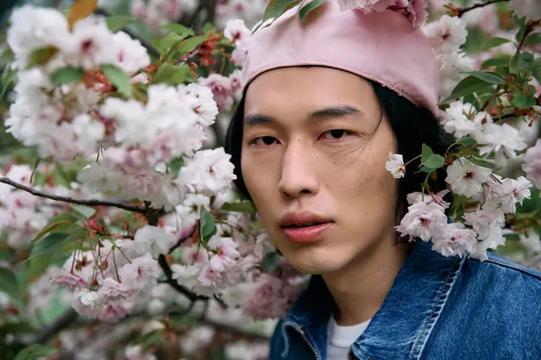 A young Asian man in a stylish denim outfit enjoys nature and vibrant flowers in the park. — Stock Photo